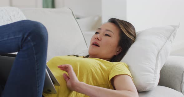 Happy asian woman lying on sofa, resting with laptop at home