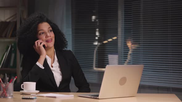 Portrait of African American Woman Texting with Client Using Laptop and Talking on Smartphone