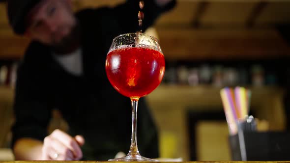 A Professional Bartender is Preparing an Alcoholic Cocktail with Ice Cubes to Customers at the Bar