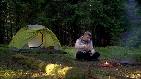 A Man Drinks Coffee Near a Tent in the Forest