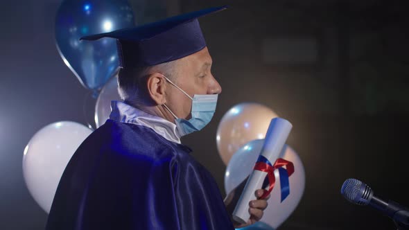 Male Rector Wearing Medical Mask Wearing an Academic Cap and Mantle Conducts Graduation Ceremony Via