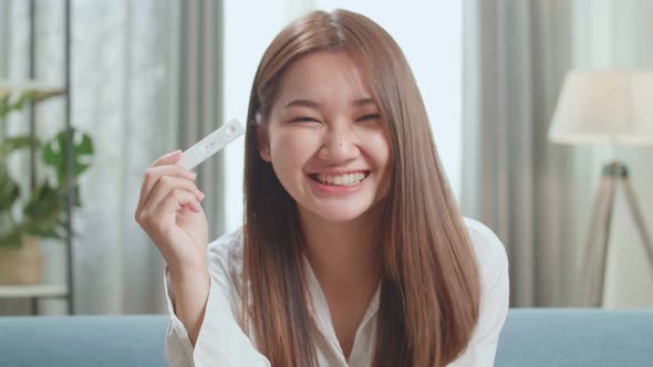 Happy Young Asian Woman Holding Pregnancy Test And Warmly Smiles To Camera