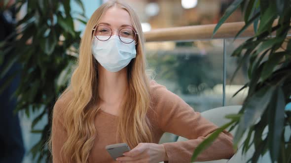 Caucasian Successful Business Woman Girl in Medical Mask Indoors with Mobile Phone Success Online