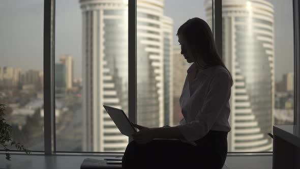 Silhouette of Businesswoman Working on Laptop in Office Near Window. Girl Working Alone in the