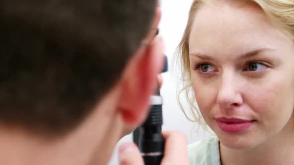 Optometrist examining female patient through ophthalmoscope