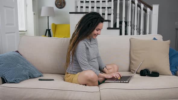 Pregnant Woman which Sitting on the Couch at Home and Remotely Working on Laptop