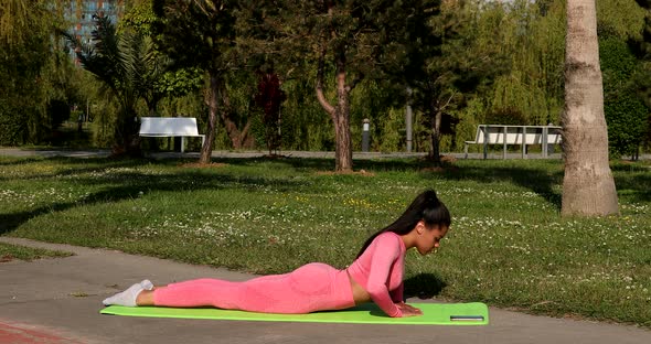 Beautiful slim young woman sitting on yoga mat on sunny day and stretching.