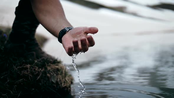 Man picks up water in his hand from a mountain lake with crystal clear water