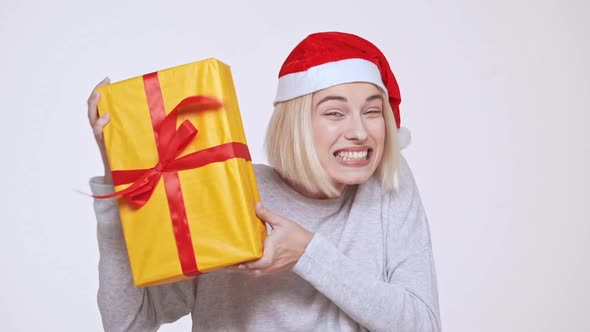 Young Beautiful Excited Blonde Girl in Christmas Hat Holding Gift Box White Background Slow Motion