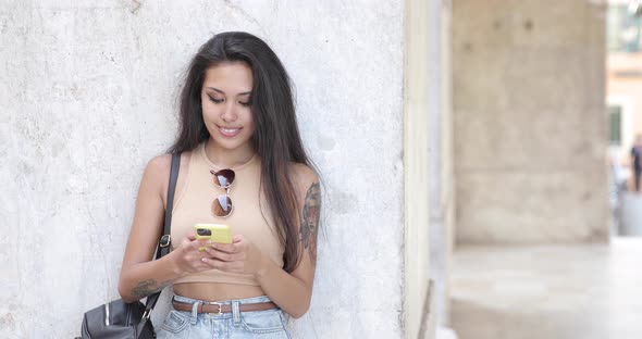 Black-haired woman using smartphone leaning on wall