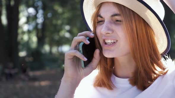 Portrait of Pretty Positive Teenage Girl with Red Hair Wearing Straw Hat and Pink Earphones Talking