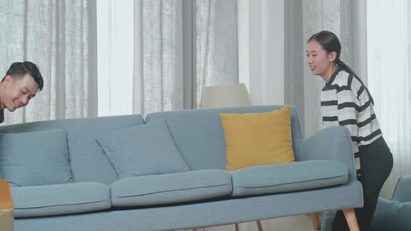 Young Asian Couple Moving New Sofa Into A New House Before Sitting On It To Rest