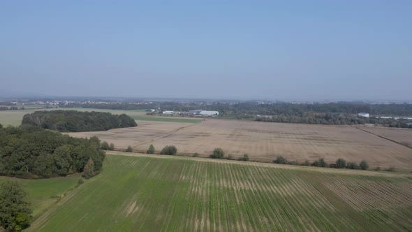 Aerial view flying over cultivated farmland with the village of Cresnjevec, Slovenia, in the distanc