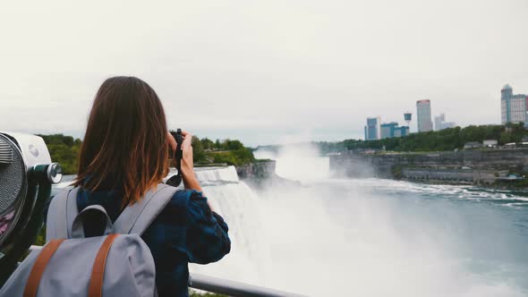Back View of Happy Traveler Woman with Backpack and Camera Taking Photo of Amazing Niagara Falls
