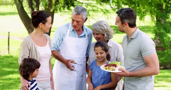 Happy Grandfather Serving Burgers at Family Barbecue in the Park