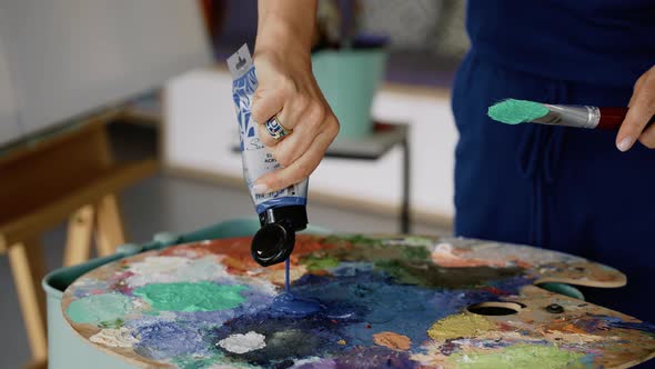 Unrecognizable woman pouring blue paint on a painting palette