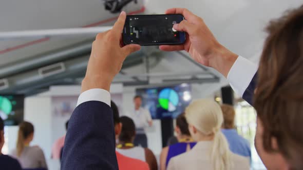 Man in audience at a business conference filming with smartphone