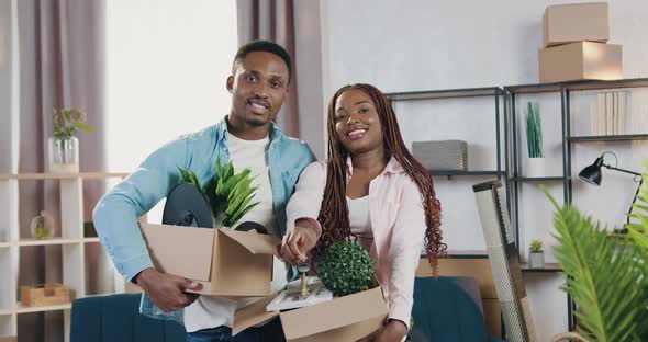African American Couple Holding Carton Boxes with Flowers and Looking at Camera