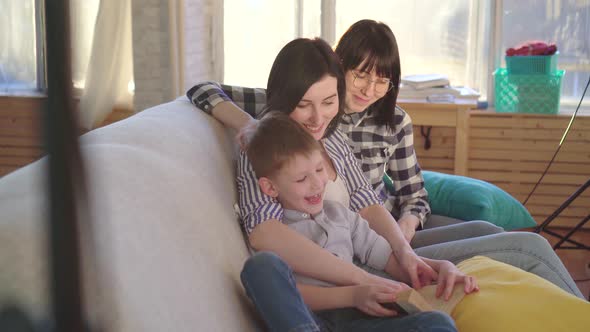 Two Happy Young Women and a Little Boy Reading a Book Close Up