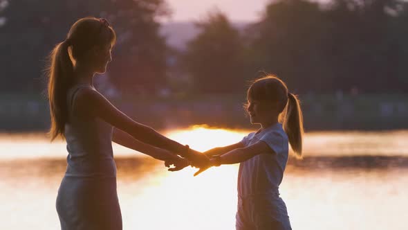Happy Mother and Daughter Standing Together Holding Hands Enjoying Time in Summer Park in Evening
