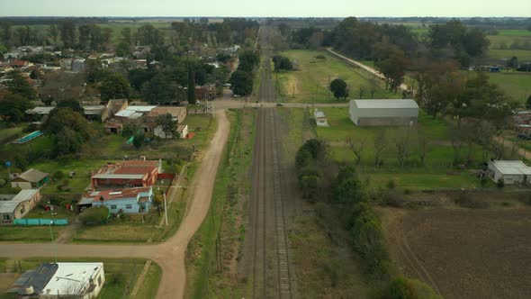 Aerial: slowly moving forward over railway tracks, afternoon rural town, countryside, Argentina.