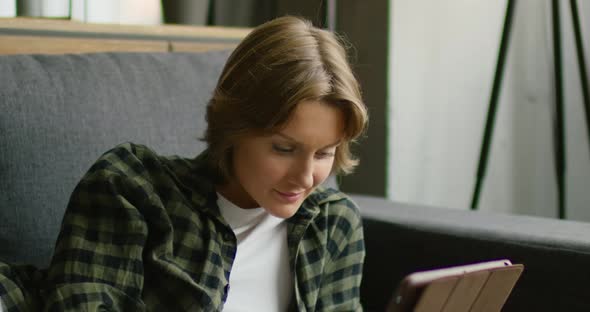 Young Woman Is Lying on Sofa, Using Tablet Computer, Close Up