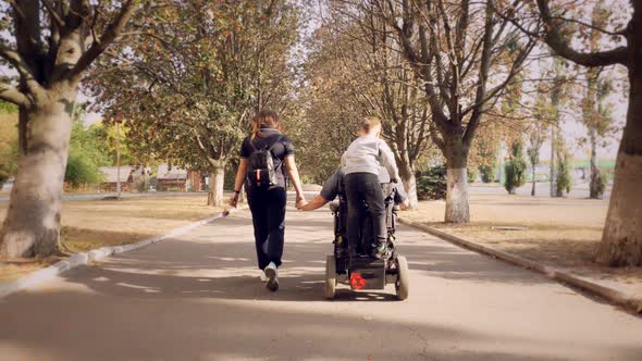 Wheelchair Man. Handicapped Man. Young Disabled Man in an Automated Wheelchair Walks with His Family