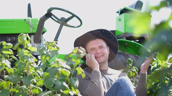 A Young Farmer Uses a Smartphone He is Resting Near His Tractor