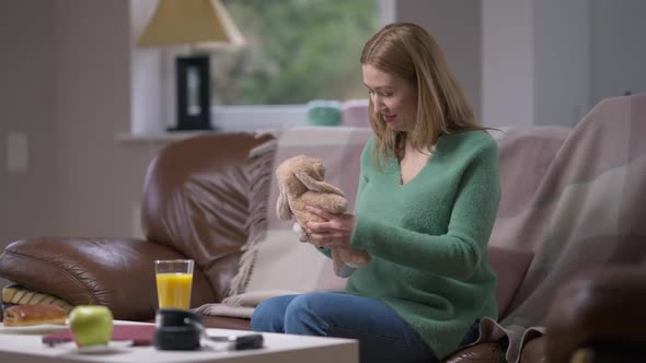 Positive Young Pregnant Woman Sitting in Living Room Talking with Toy Rabbit in Slow Motion Smiling