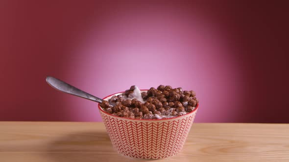 Spoon Falls Into a Deep Bowl Filled with Chocolate Corn Balls and Milk