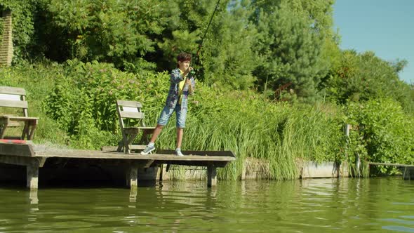 Skillful School Age Boy with Fishing Rod Enjoying Fishing From Jetty on Lake