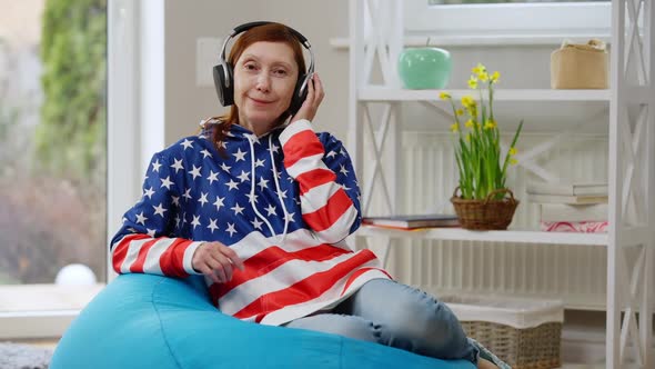 Happy Mature Woman in Hoodie Colored As USA Flag Looking at Camera Smiling Sitting on Bag Chair