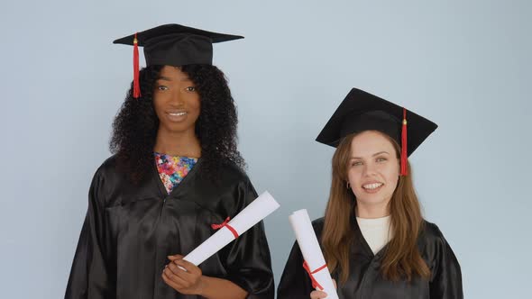 Young African American and Caucasian Women Stand Side By Side and Hold Diplomas in the Middle