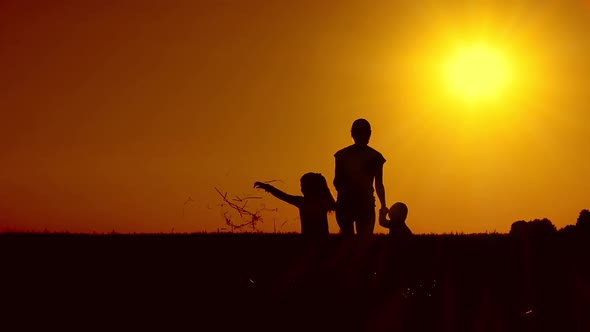 Silhouettes at sunset. Mother daughter and son are on the field . The concept is a happy family.