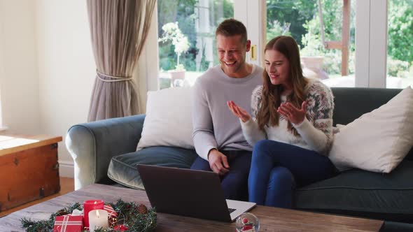 Caucasian couple smiling while having a video call on laptop sitting on the couch at home