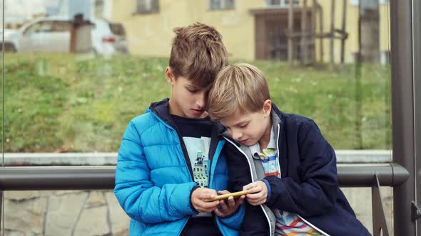 Two Boys Are Sitting At The Bus Stop.