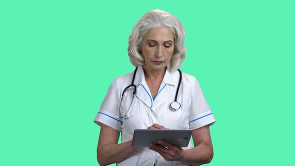 Mature Female Doctor Using Pc Tablet on Color Background.