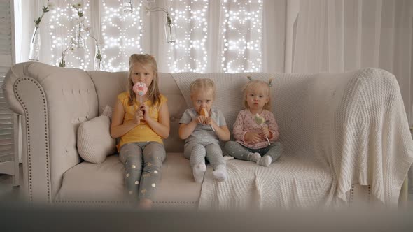 Three Funny Kids Sitting on Sofa and Eating Sweet Snack on Stick