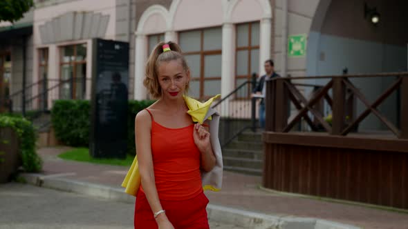 a Woman in Red Clothes Has Thrown a Yellow Jacket Over Shoulder and is Walking Backwards Along a