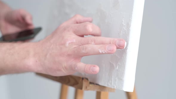 The Artist Applies a Plaster Base on a White Canvas