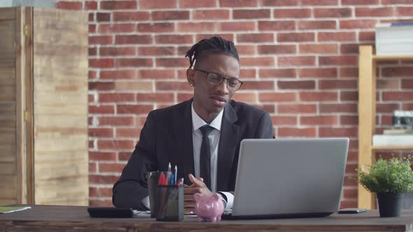 Black Man in Suit and Tie at the Office Table Speaks By Video Link on a Laptop and Negative