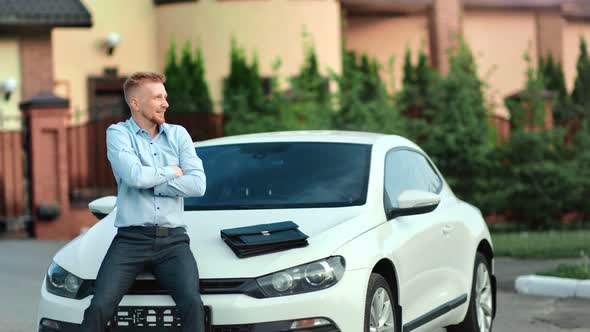 Happy Successful Young Business Male Making Winner Gesture Rising Up Hand Sitting on Car Bonnet