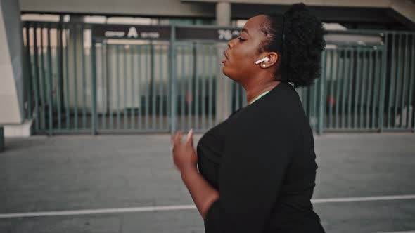 Close Up Portrait of Overweight African American Woman in Wireless Headphones Running Alone