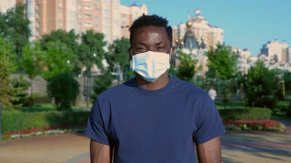 Portrait Smiling AfroAmerican Man in Protective Medical Face Mask Looks Camera