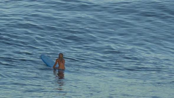 A young woman surfing in a bikini on a longboard surfboard.