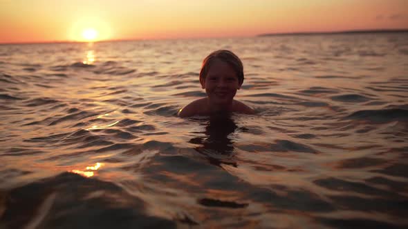 Portrait of Young Caucasian Boy 1012 Swimming in Sea Alone and Looking at you During Amazing Dusk in