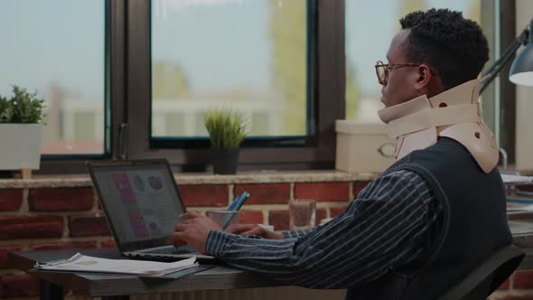 Injured Worker with Cervical Collar Using Laptop to Plan Finance
