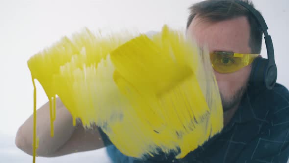 Man with Headphones Paints Wall with Yellow Color in Room