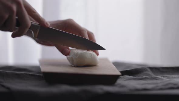 Slow Motion Man Slicing Mozzarella Ball on Olive Wood Board with Window on Background