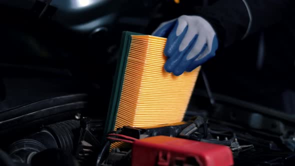 Man with gloves inserts a new air filter into a car in a service station